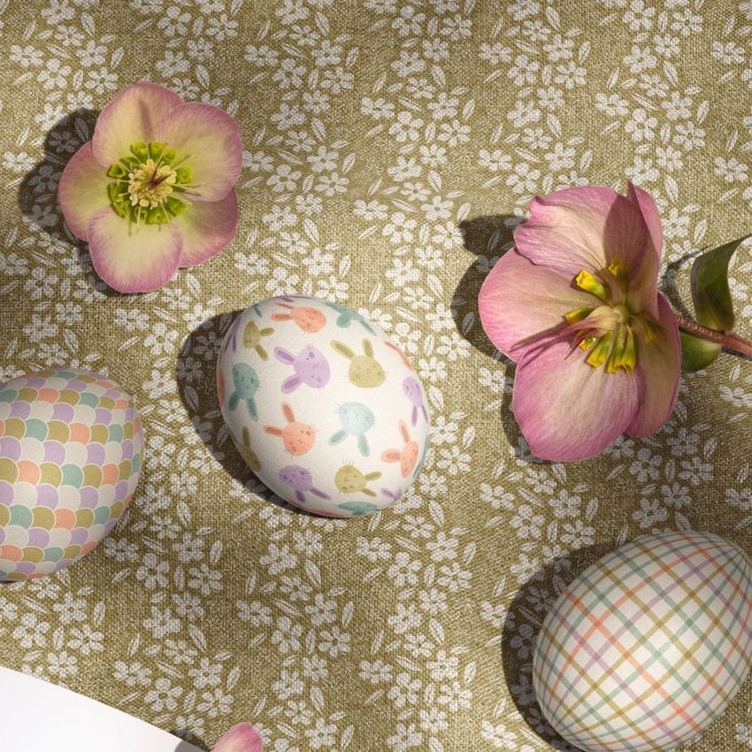 Easter eggs mockup featuring three decorated eggs with pastel patterns and two pink flowers on a green floral fabric background.