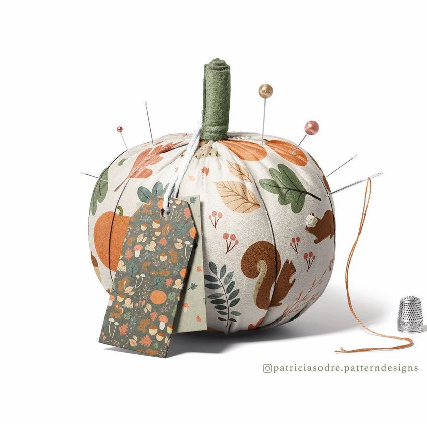 Fabric pumpkin mockup decorated with autumn-themed patterns, used as a pincushion with pins and a tag attached.
