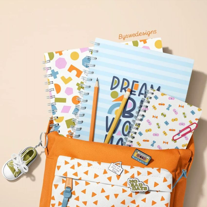 School backpack mockup with spiral notebooks featuring playful geometric patterns, pencils, and a small sneaker keychain on a beige background.