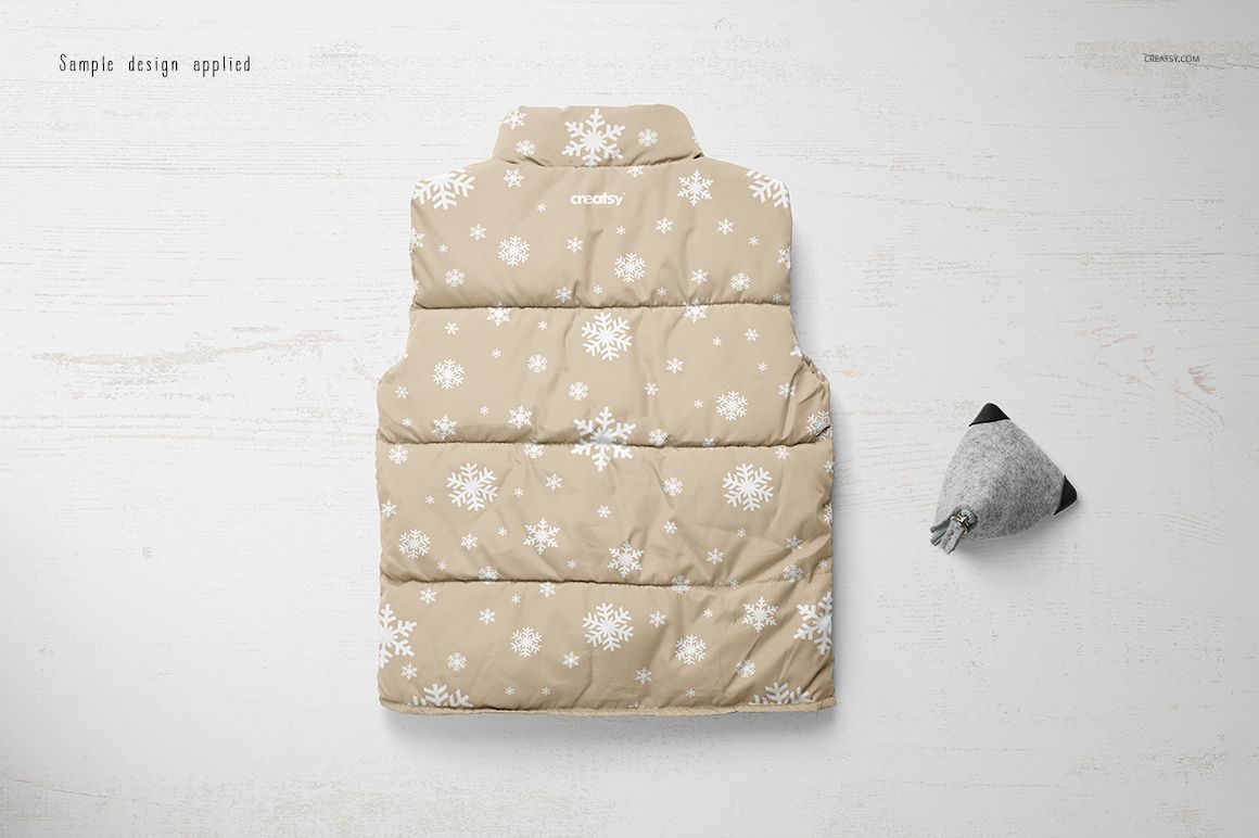 PSD mockup showing a beige boys winter vest with white snowflakes, laid flat next to a small gray plush toy.