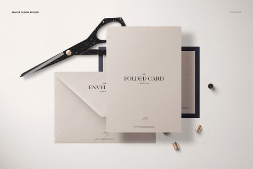 Folded card and envelope mockup set displayed on a light surface with scissors and small metallic props nearby.
