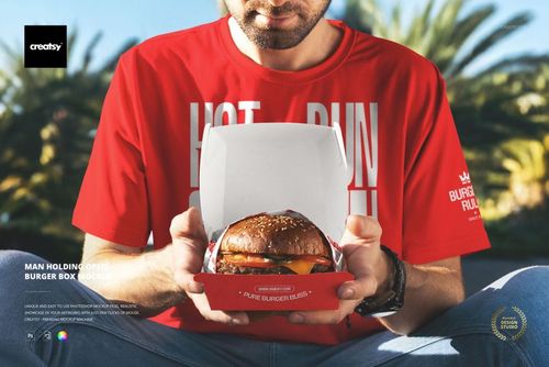 Man in a red shirt holding an open burger box mockup with a visible burger inside, shown from the front view.