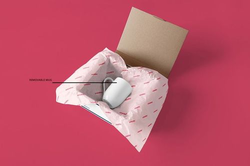 PSD mockup showing an open packaging box with branded wrapping paper and a ceramic mug, presented on a pink backdrop.