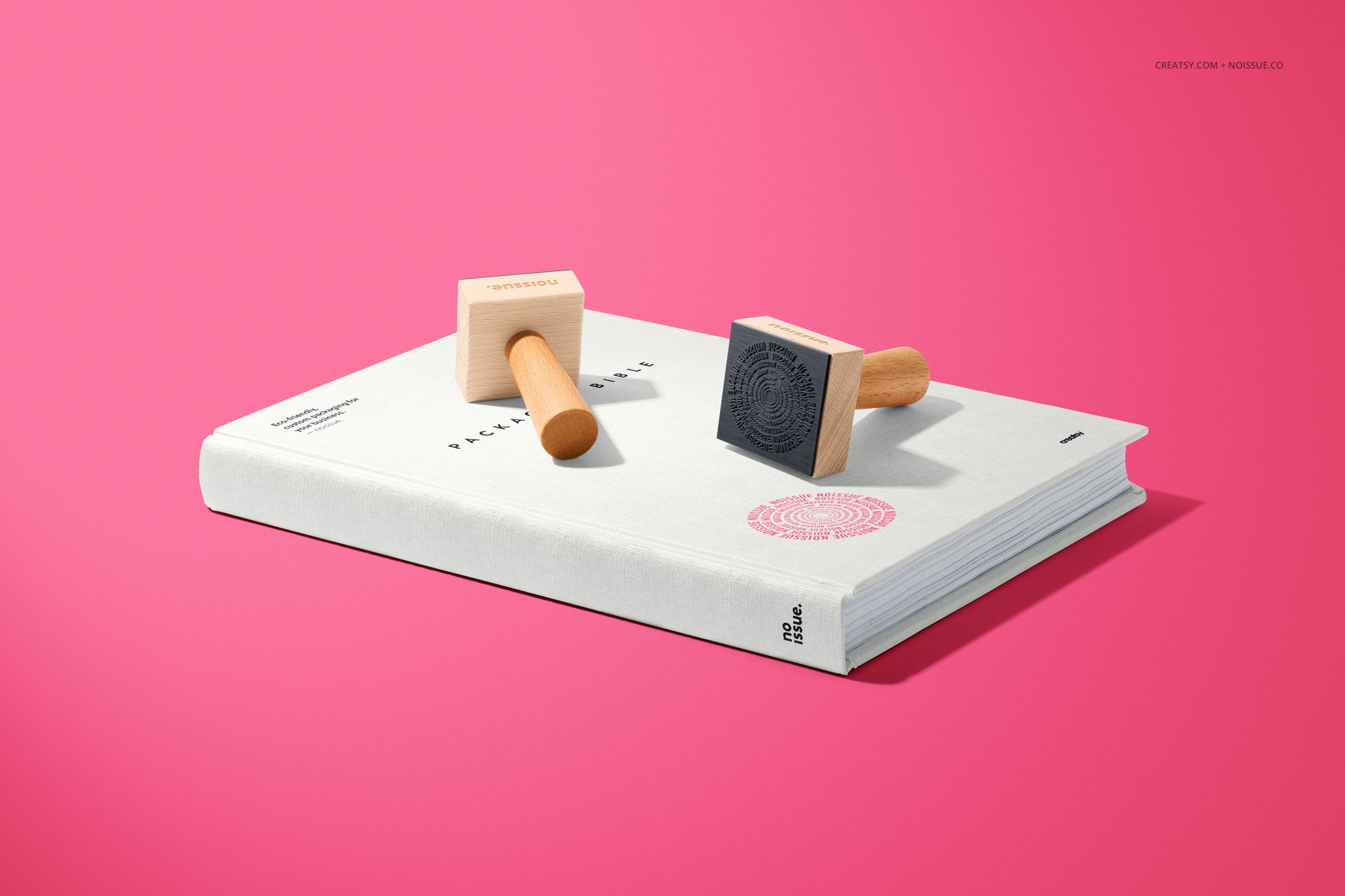 Mockup of wooden stamps positioned on a white book, featuring a pink background and minimal stationery props.