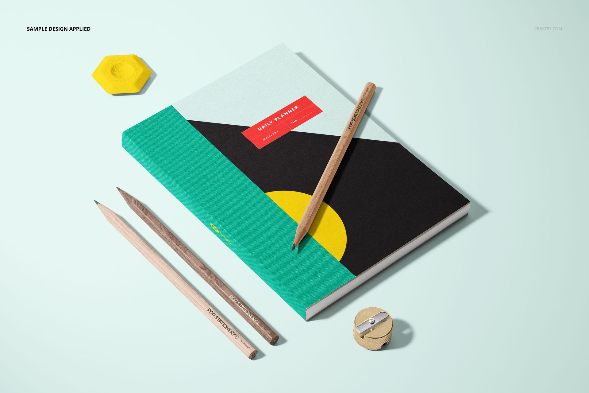 Stationery mockup showing a closed planner with colorful abstract cover, pencils, sharpener, and hexagonal eraser.
