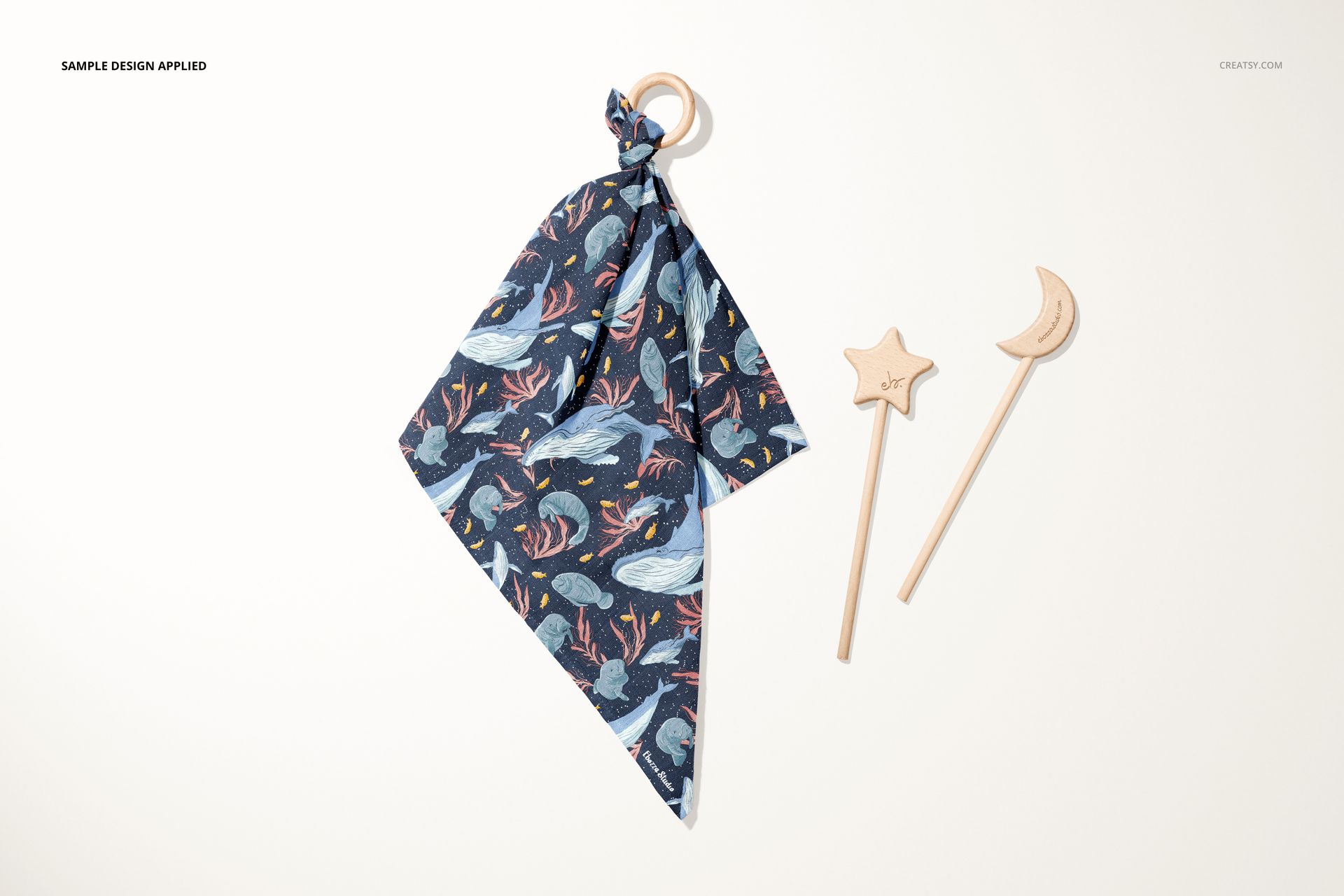 Top view of muslin cloth wooden teether mockup with ocean-themed fabric and two engraved wooden sticks shaped like a star and moon.
