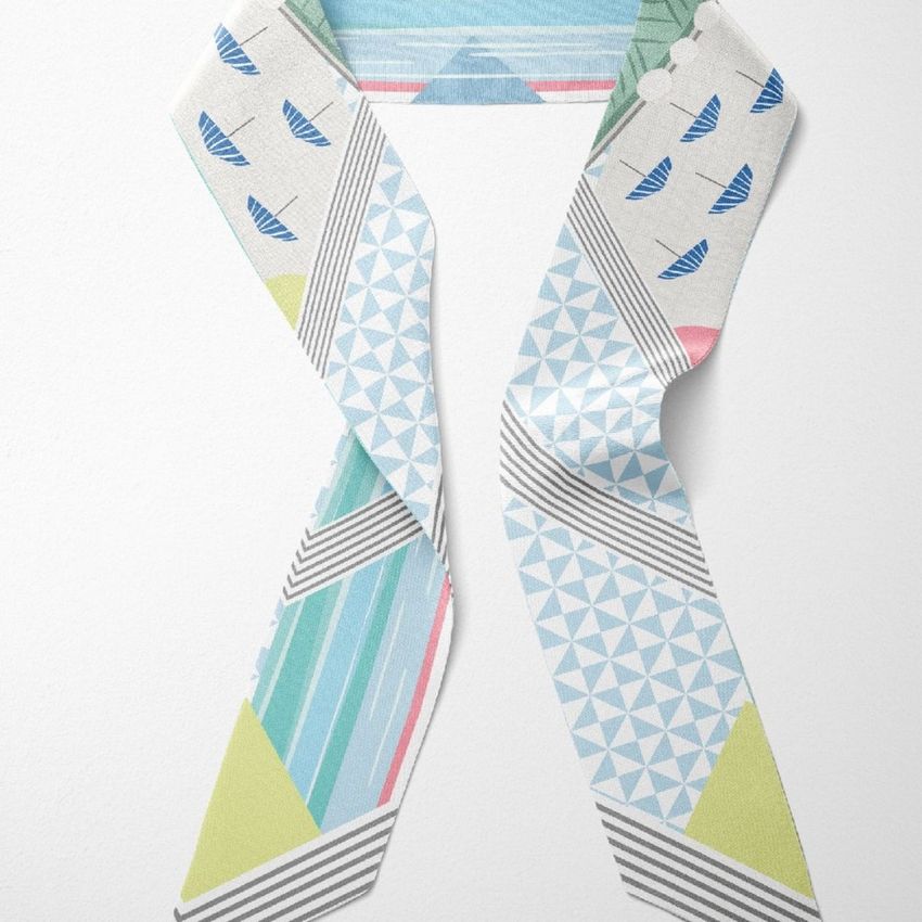 Top view of a twilly scarf mockup with geometric patterns in blue, green, and gray on a white background.