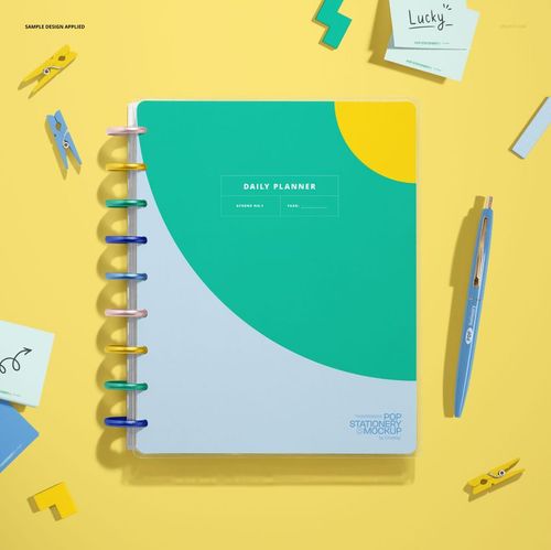 Spiral planner mockup displayed from above, featuring a green and yellow cover with assorted stationery items nearby.