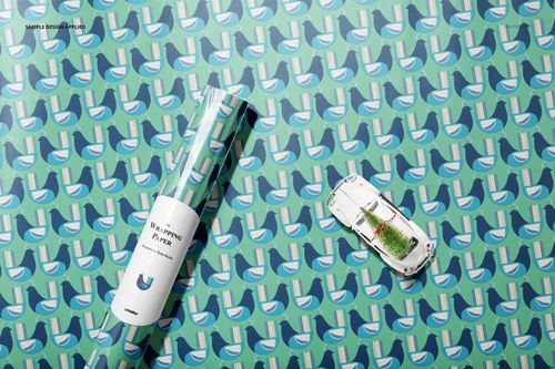 Gift wrapping paper mockup with roll and toy car on a flat surface featuring repeating green and blue geometric design.