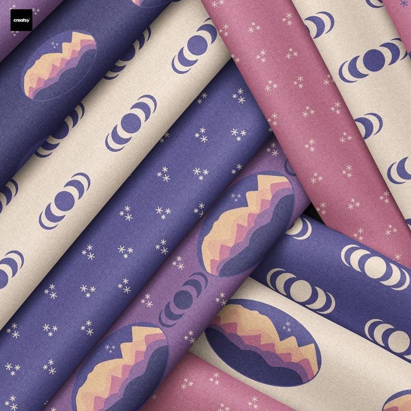Folded fabrics mockup displaying overlapping pieces with moon phases, stars, and mountain patterns in purple, beige, and pink tones.