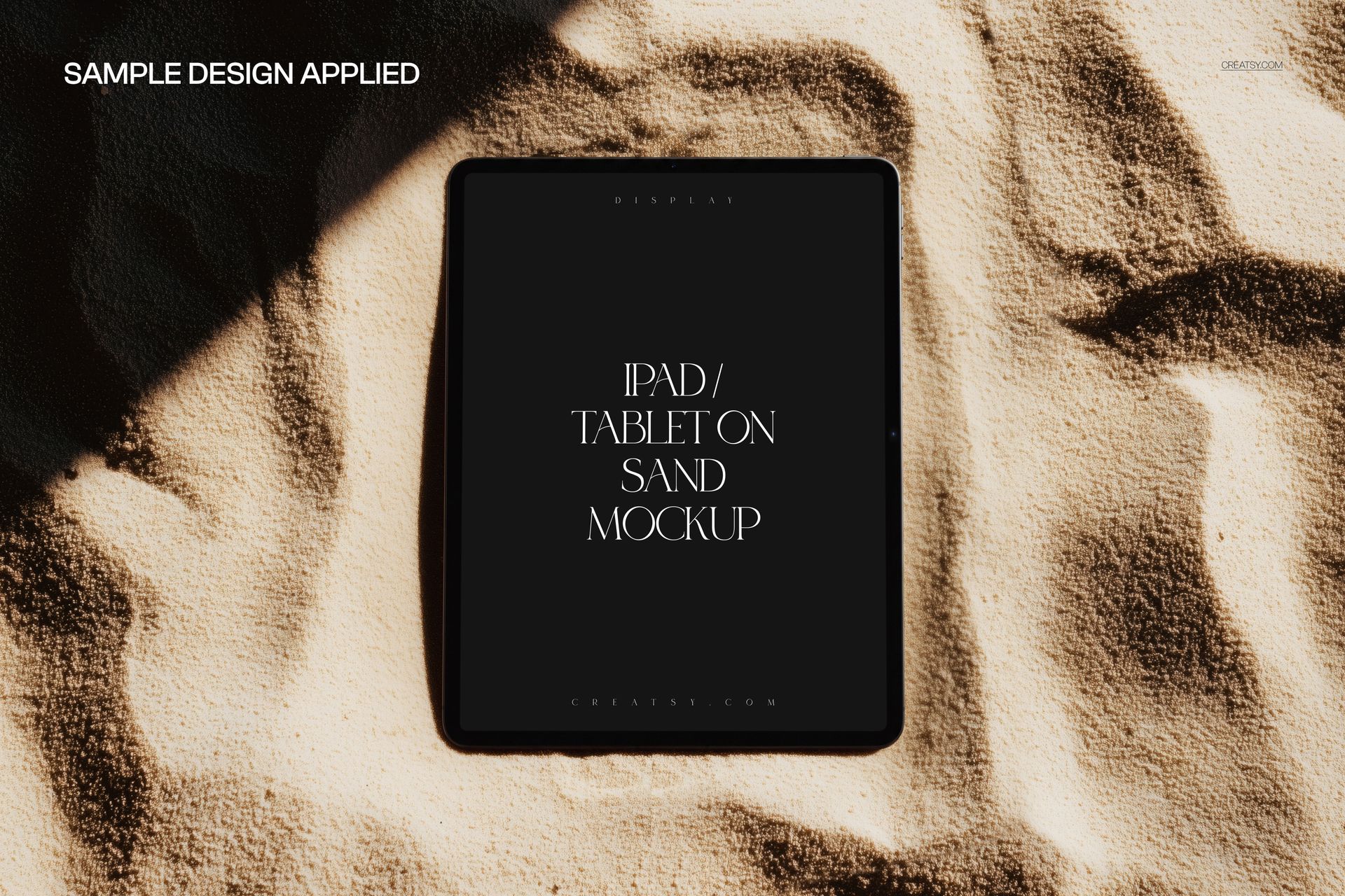 iPad Pro lying flat on textured sand surface, screen facing up with sample design, top view mockup scene.
