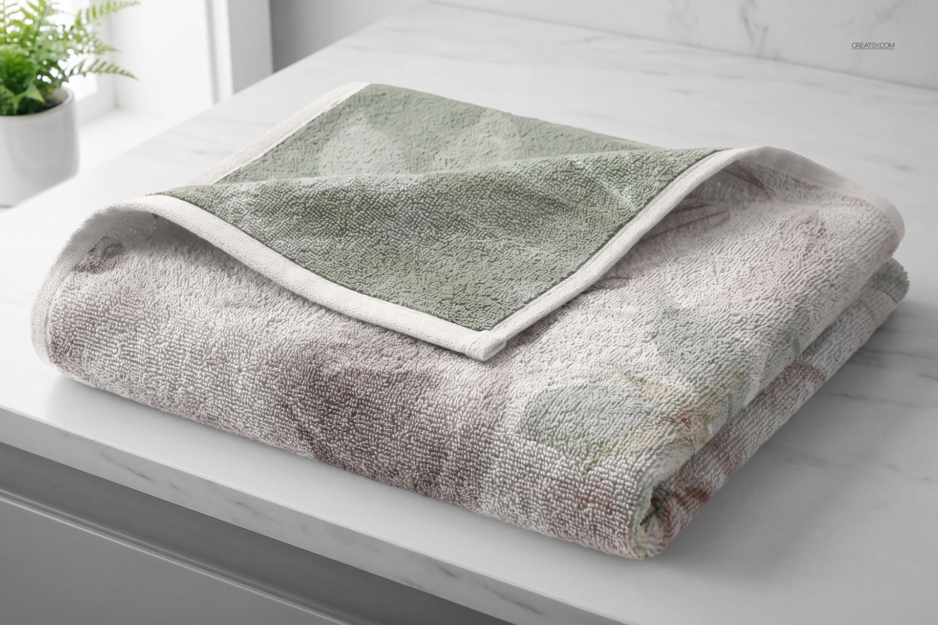 Bathroom towel mockup featuring a soft pastel floral design, shown folded on a white marble surface near a window.