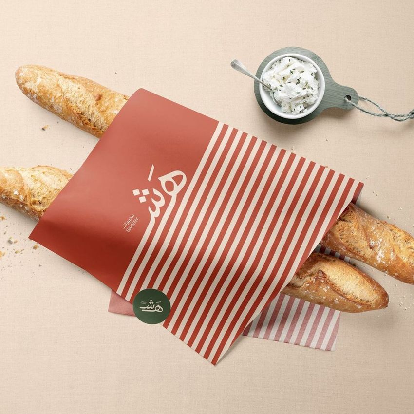Food safe paper mockup showing a red and white striped sheet partially wrapping two baguettes on a beige surface with a bowl of spread.