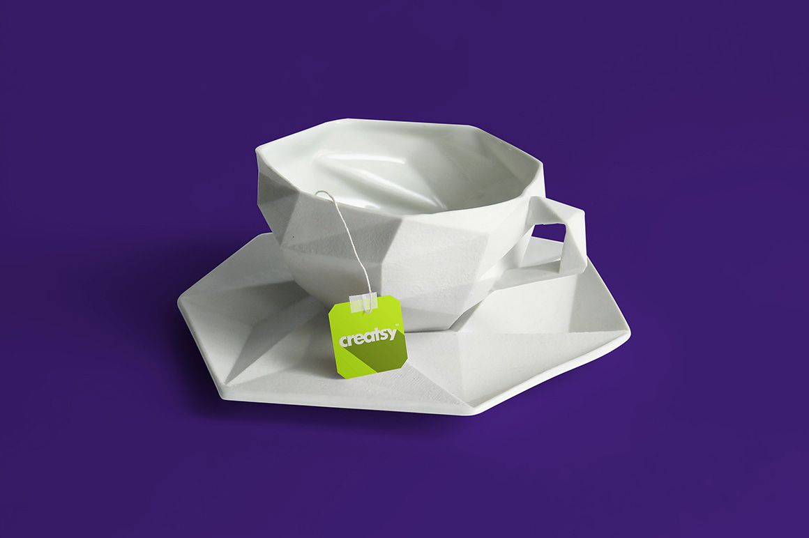 Modern faceted tea cup and saucer set with a tea bag, shown in a PSD mockup scene against a purple background.