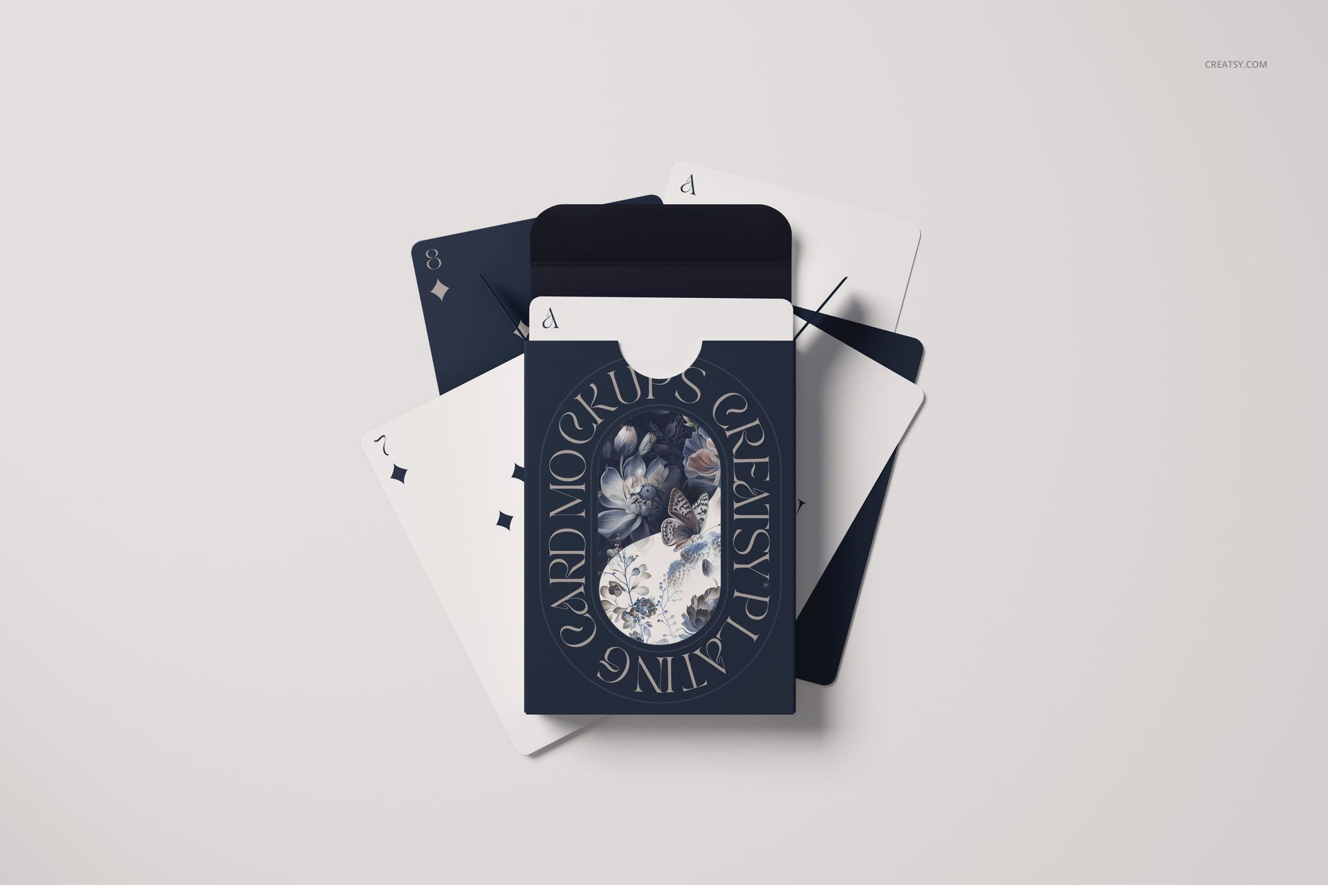 Top view of a playing cards mockup featuring a dark blue box with floral artwork and scattered cards around it.