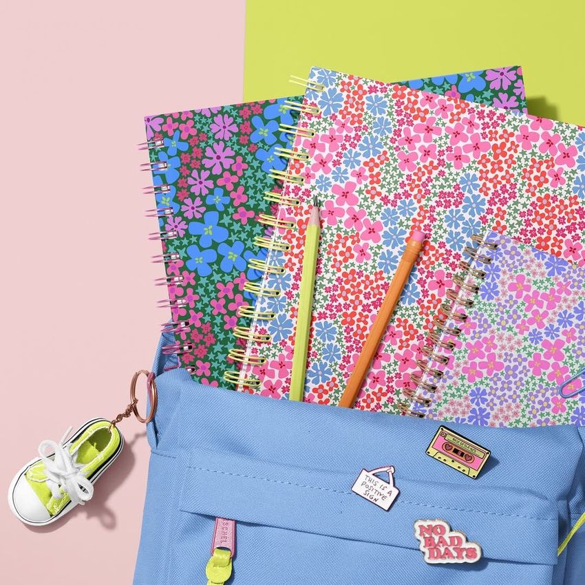 School backpack mockup with three spiral notebooks featuring colorful floral covers, two pencils, and a sneaker keychain on a pastel background.
