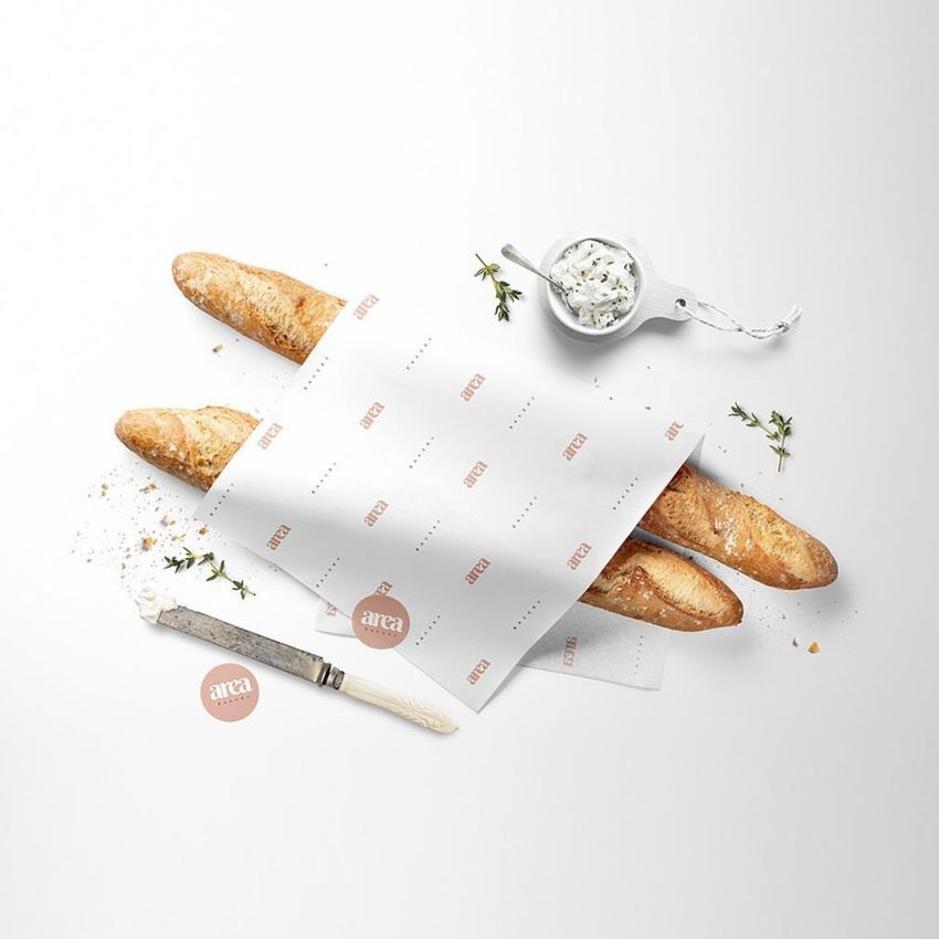 Bakery food safe paper mockup featuring two baguettes partially wrapped in patterned paper on a white surface with herbs and a knife.