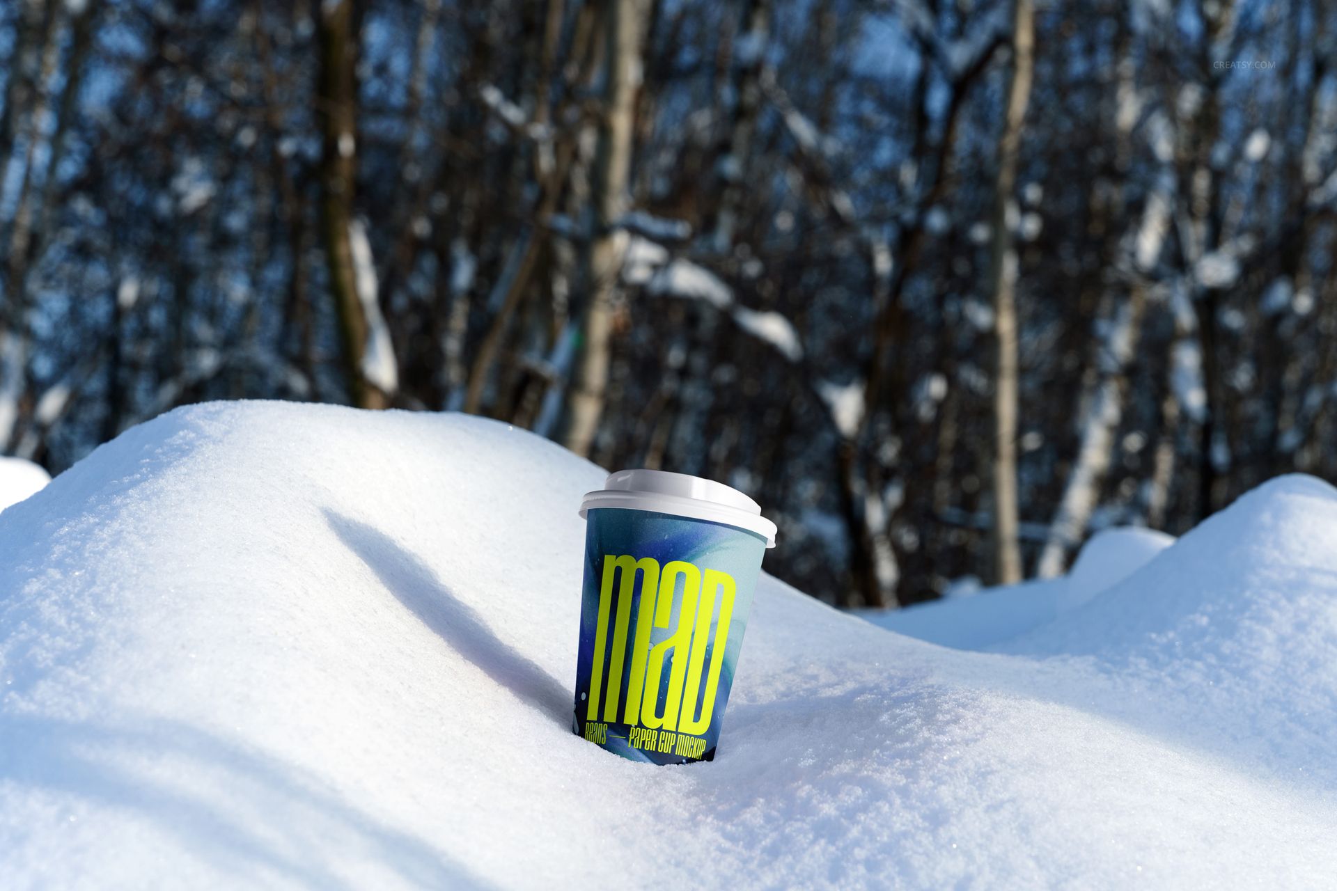 Winter-themed paper cup mockup featuring a colorful cup with lid placed on a snowy surface, forest visible behind.