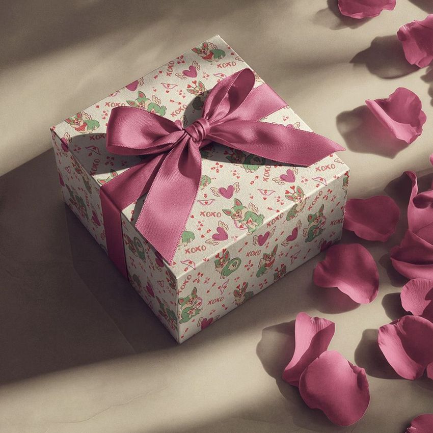 Square gift box mockup with a pink ribbon bow, decorated with playful patterns and surrounded by scattered rose petals.