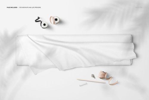 Top view of a fabric bolt mockup with white cloth draped, surrounded by sewing accessories on a light surface.