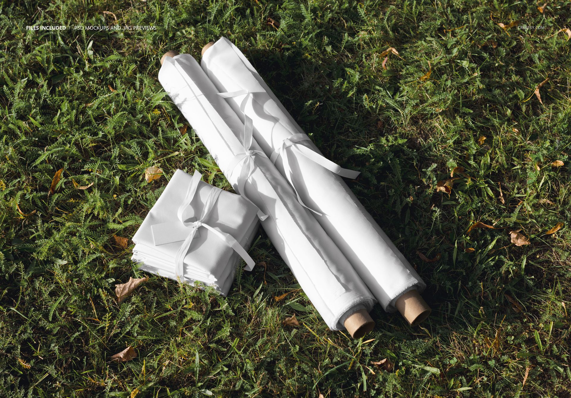 PSD mockup showing fabric rolls and a rectangular stack on outdoor grass, with natural sunlight and shadows.