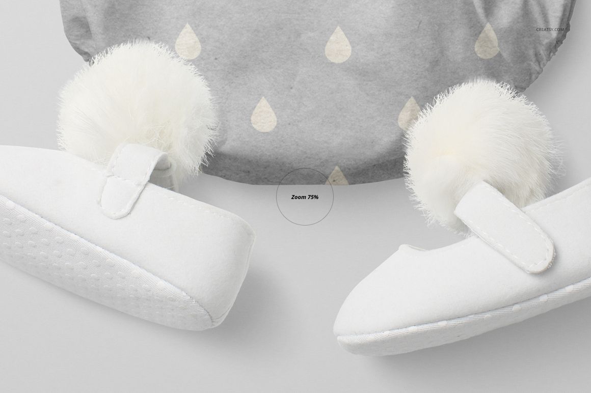 Close-up view of a baby romper mockup with a gray fabric and subtle drop pattern, paired with white baby shoes featuring fluffy pom-poms.