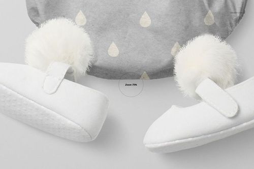 Close-up view of a baby romper mockup with a gray fabric and subtle drop pattern, paired with white baby shoes featuring fluffy pom-poms.