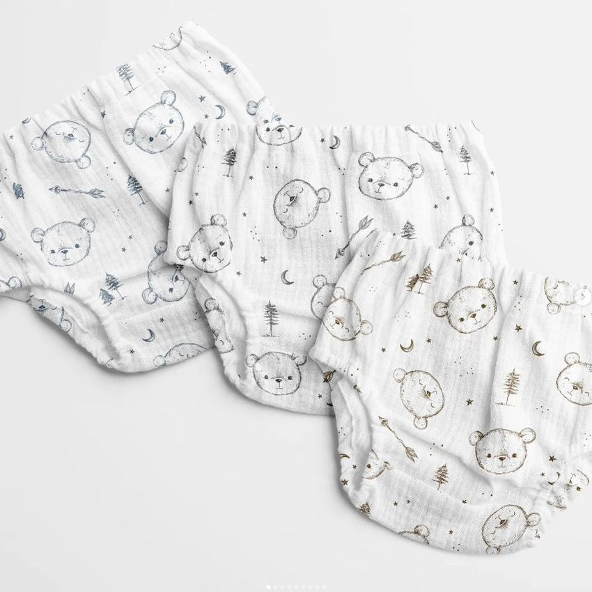 Three baby muslin pants mockups with sketchy bear faces, trees, and moon patterns are arranged on a light background.