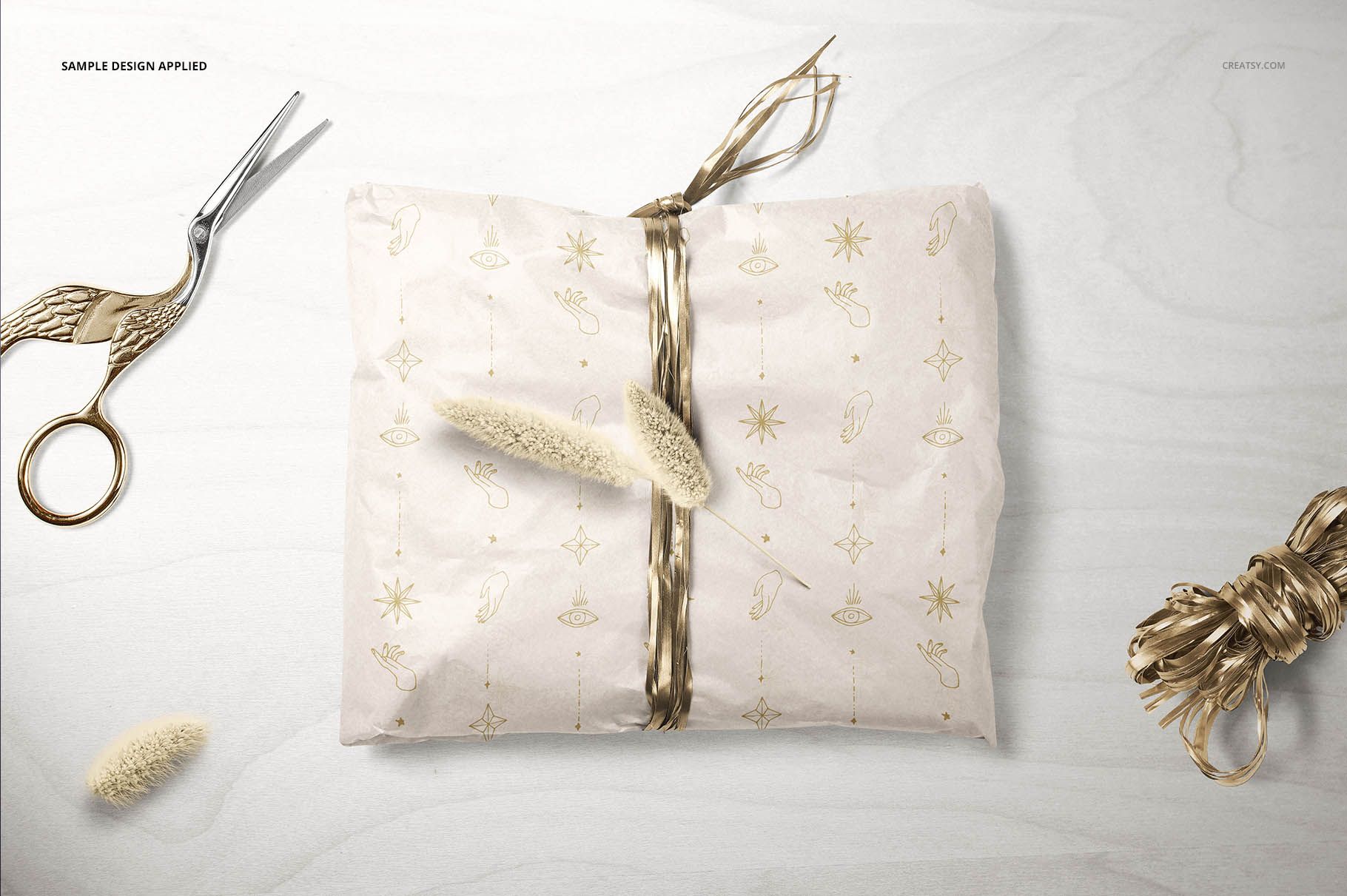 Gift wrapping tissue paper mockup featuring a rectangular parcel, gold ribbon, and decorative scissors on a table.