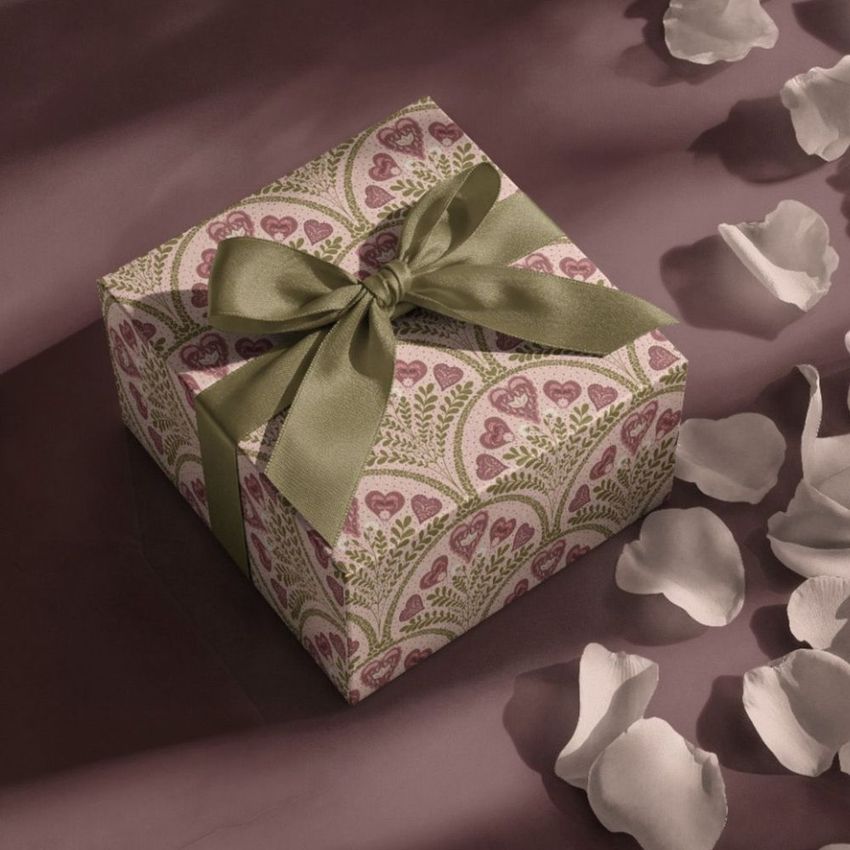 Square gift box mockup with a green ribbon, decorated with a pink and green heart pattern, surrounded by white petals.