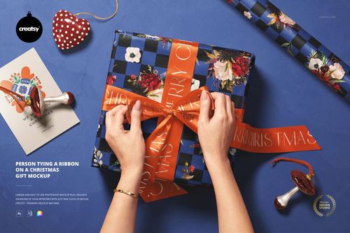 Blue floral gift box with orange ribbon being tied, shown in a Christmas PSD mockup scene with seasonal accessories.