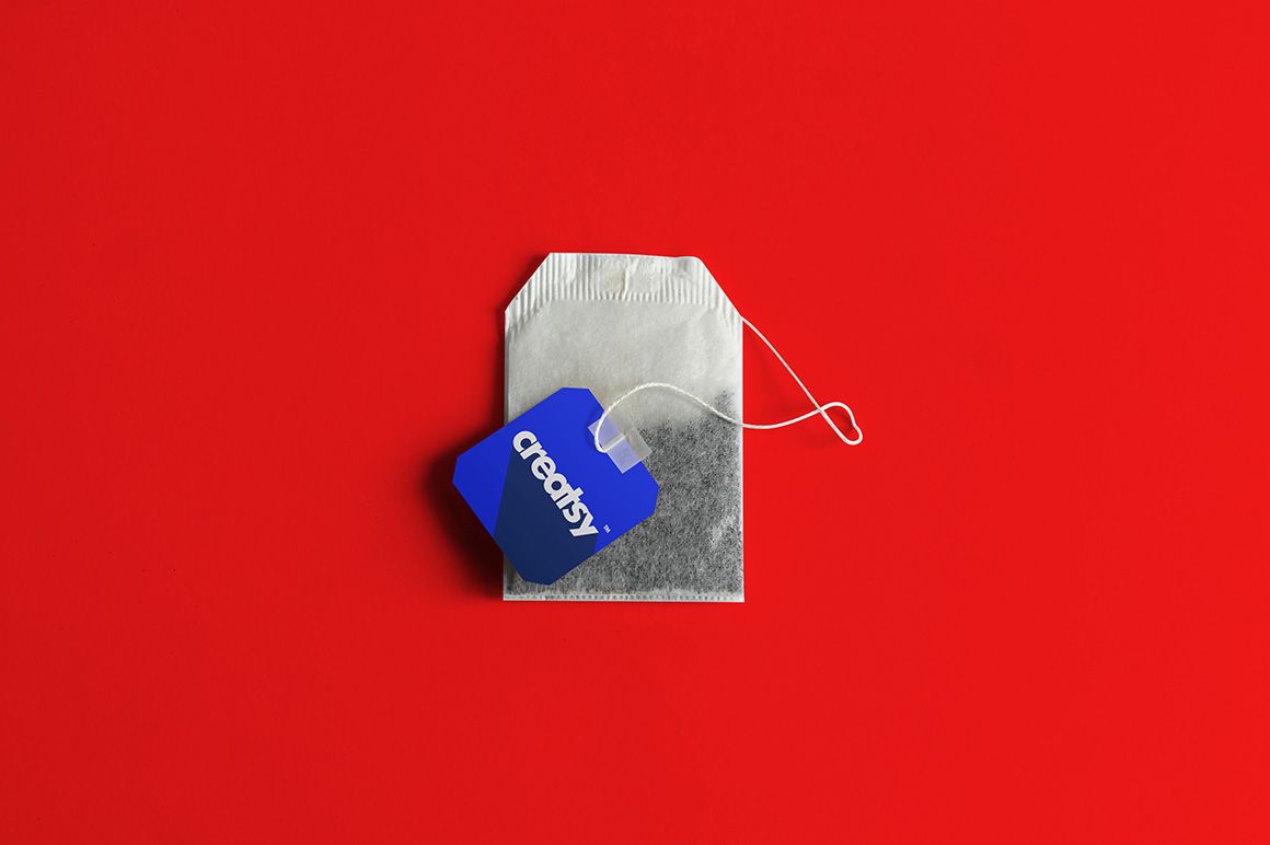 Tea bag mockup shown from above with a blue label and white text, set against a plain red backdrop.