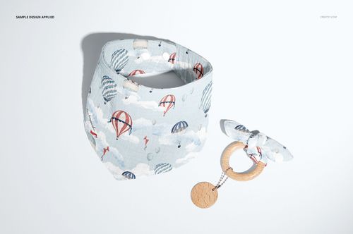 PSD mockup of a baby muslin bandana and teething ring with fabric bow, displayed on a plain surface with soft shadows.