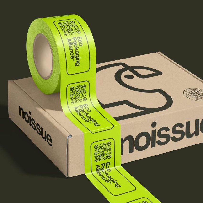 Mailing box mockup with a bold black logo on a natural cardboard surface, paired with a roll of bright green adhesive labels.