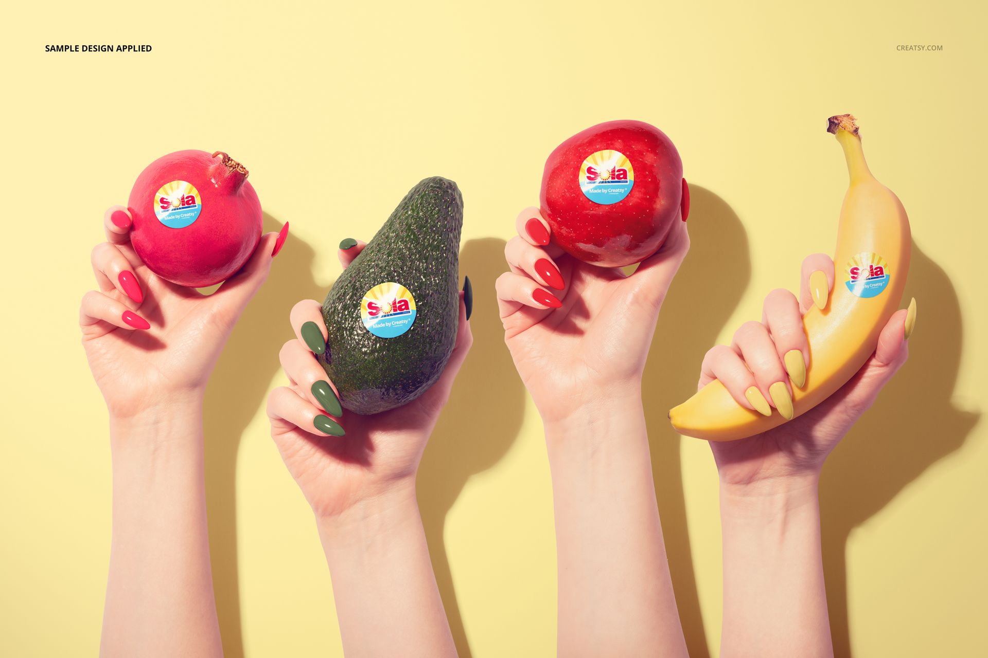 PSD mockup featuring pomegranate, avocado, and banana, each with a round sticker, held by hands on a yellow surface.