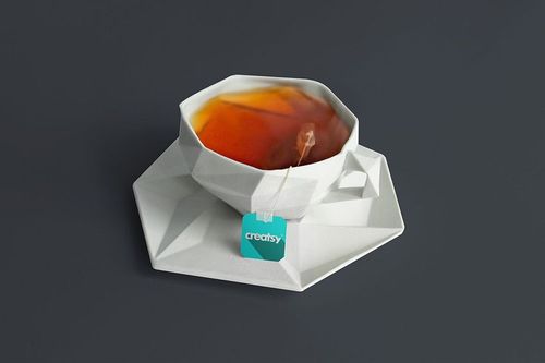 Tea cup mockup featuring faceted white ceramic design, tea bag tag visible, and dark tea inside on gray backdrop.