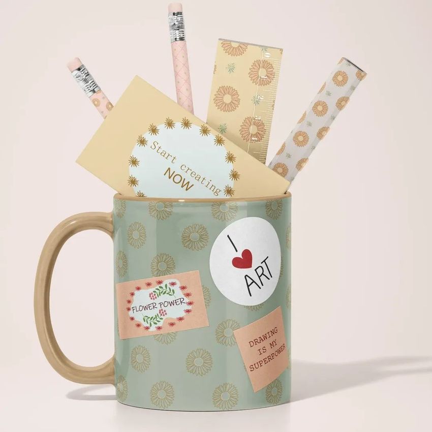 Mug mockup with a floral pattern holds pastel pencils, a ruler, and notecards on a light background with soft shadows.