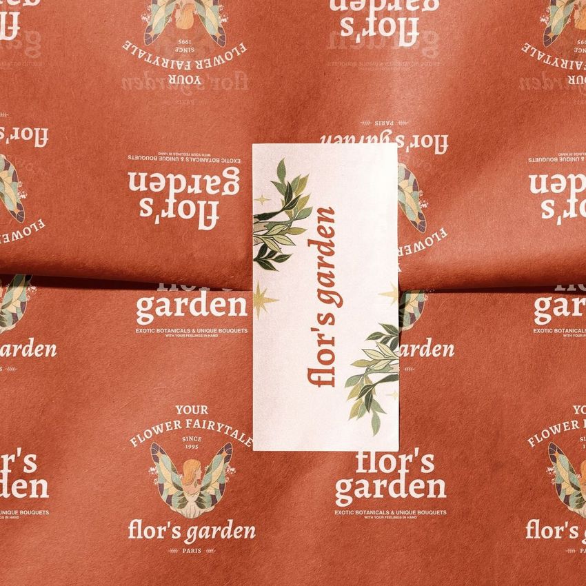 Sticker mockup featuring a rectangular label with botanical graphics and text on a folded, rust-colored floral wrapping paper.