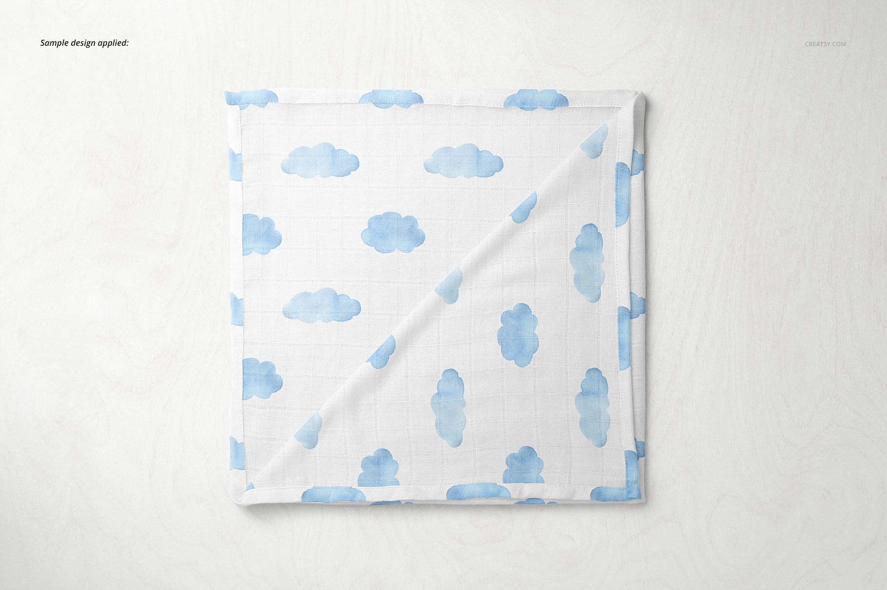 Baby muslin square nappy mockup featuring a folded white cloth with blue cloud pattern on a light surface.