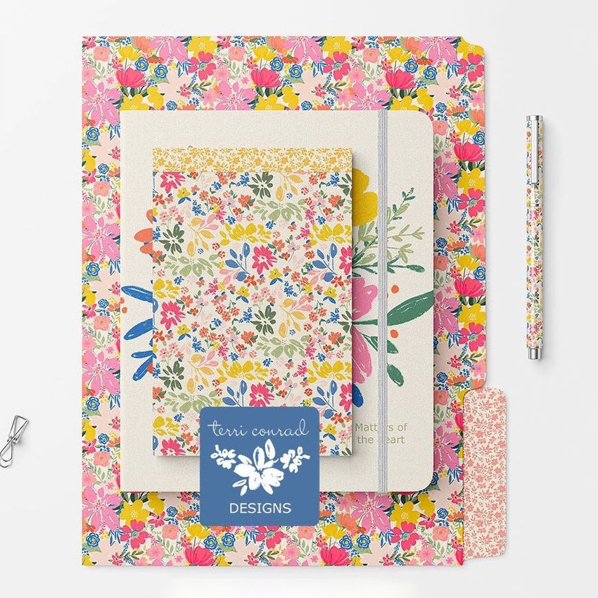 Stationery mockup featuring a floral patterned notebook, folder, pen, and paperclip arranged on a white background.