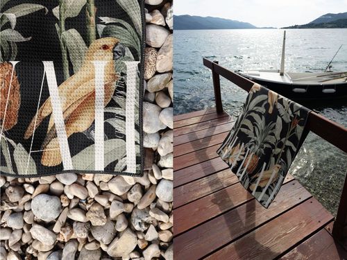 PSD mockup of a waffle beach towel featuring a botanical and bird design, displayed on rocks and beside a Croatian coastline.