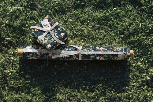 PSD mockup showing a fabric roll and folded bundle with botanical print lying on grass, overhead perspective.