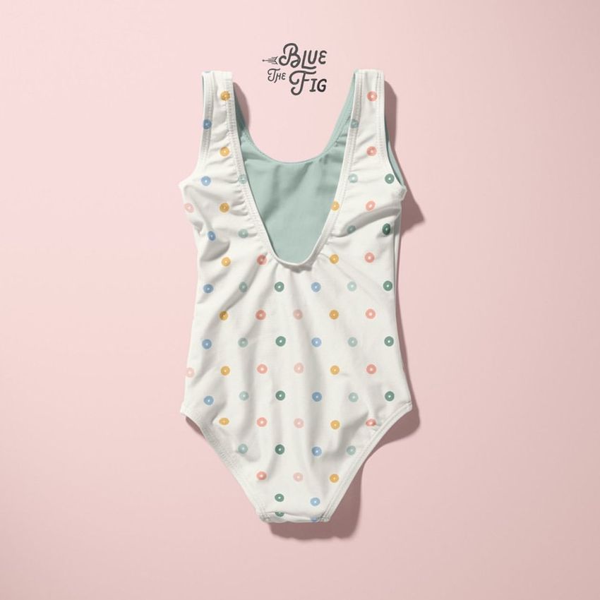 Baby swimsuit mockup featuring a white one-piece with colorful polka dots, displayed flat on a pale pink background.