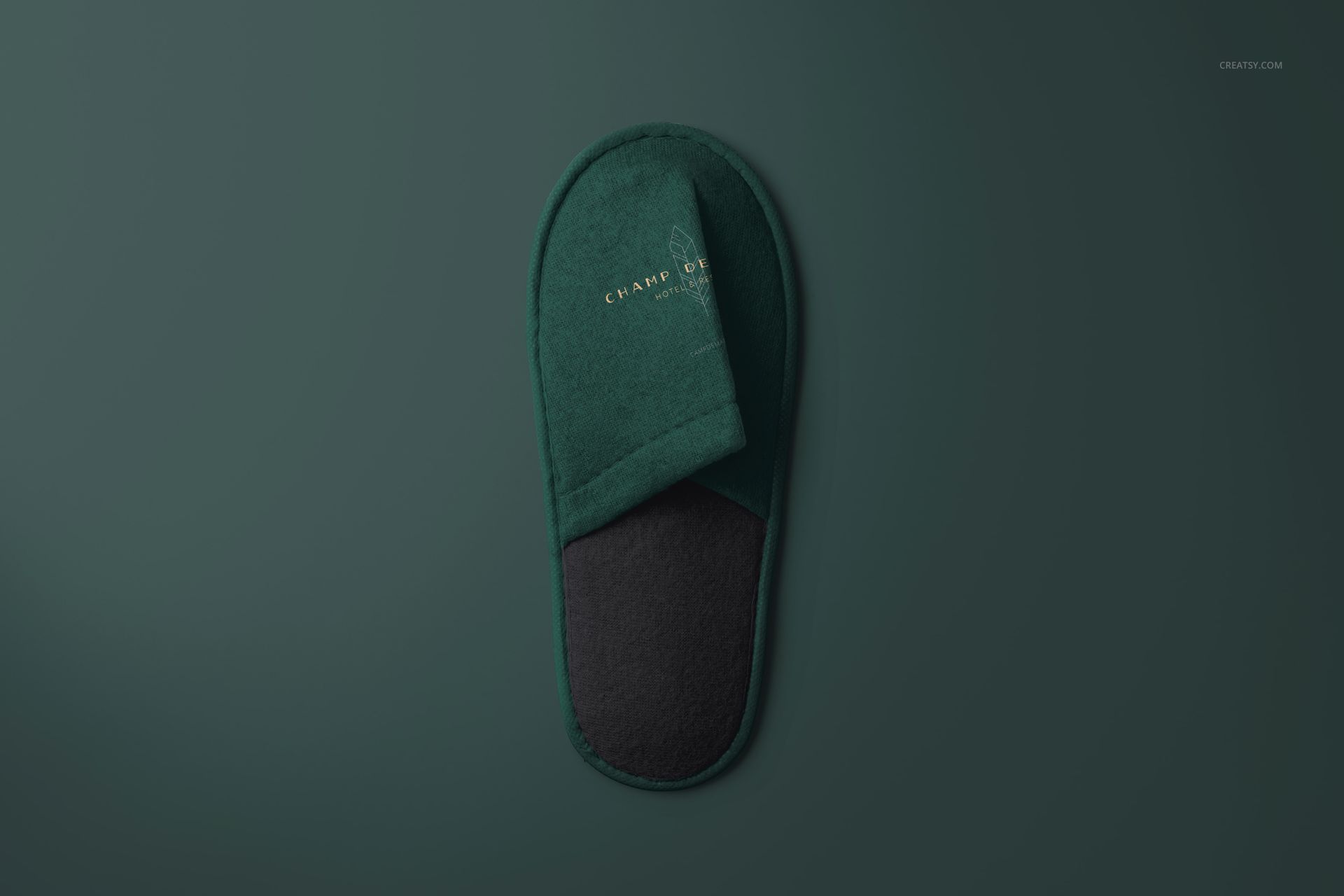 Single hotel slipper mockup in deep green with black sole, top view on a matching green background, minimal style.