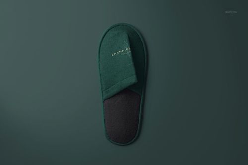 Single hotel slipper mockup in deep green with black sole, top view on a matching green background, minimal style.