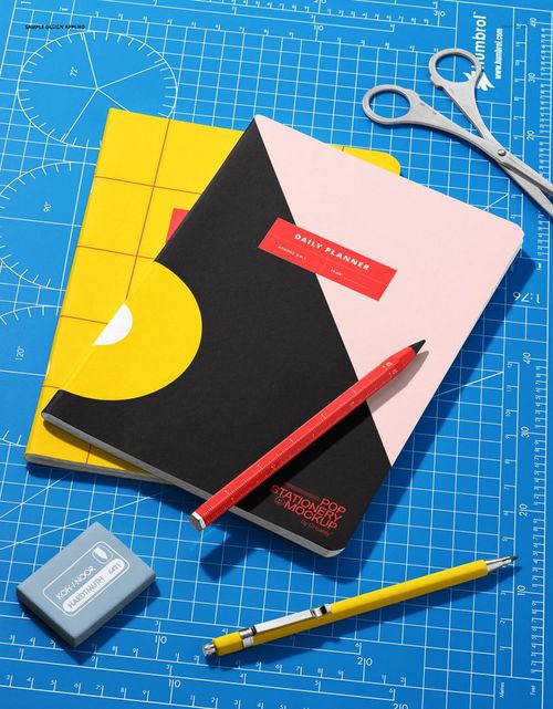 Workspace PSD mockup featuring notebooks, pencils, eraser, and scissors on a blue grid background in bright lighting.