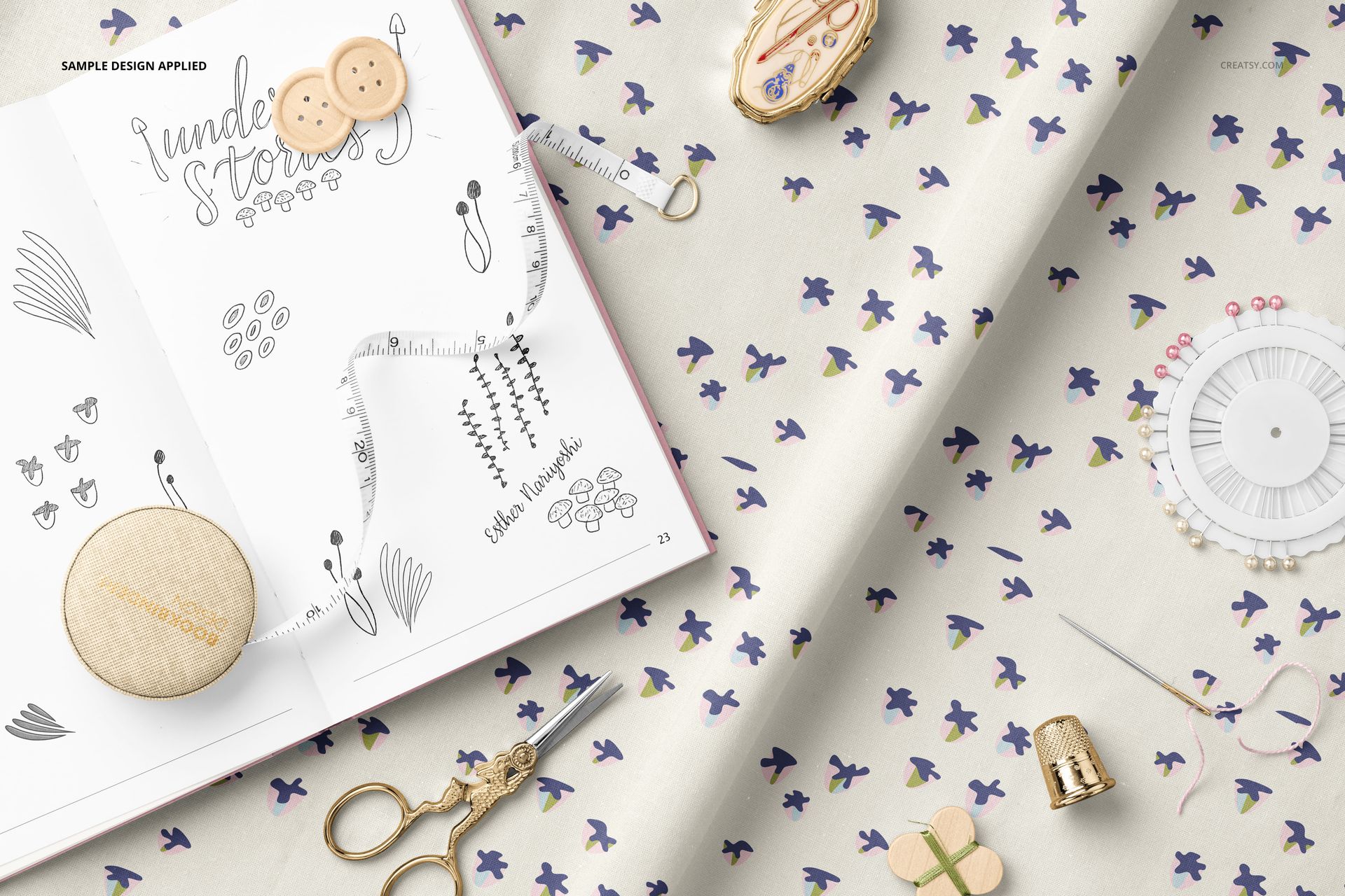 PSD mockup showing cotton fabric with a delicate floral print, surrounded by a sketchbook and various sewing supplies.