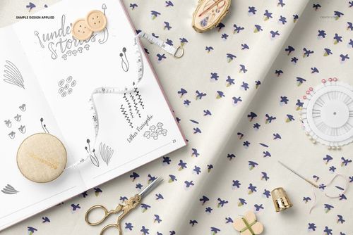 PSD mockup showing cotton fabric with a delicate floral print, surrounded by a sketchbook and various sewing supplies.