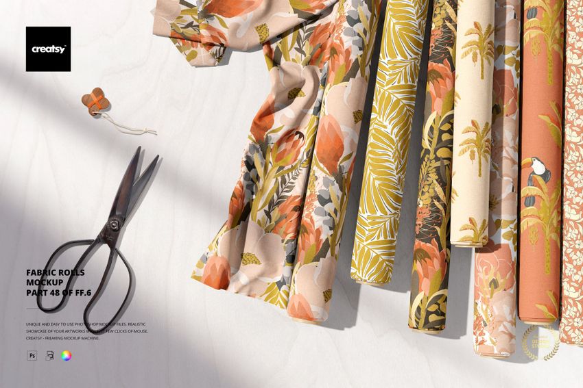PSD mockup showing assorted fabric rolls with orange, beige, and green designs, displayed on a light textured table.