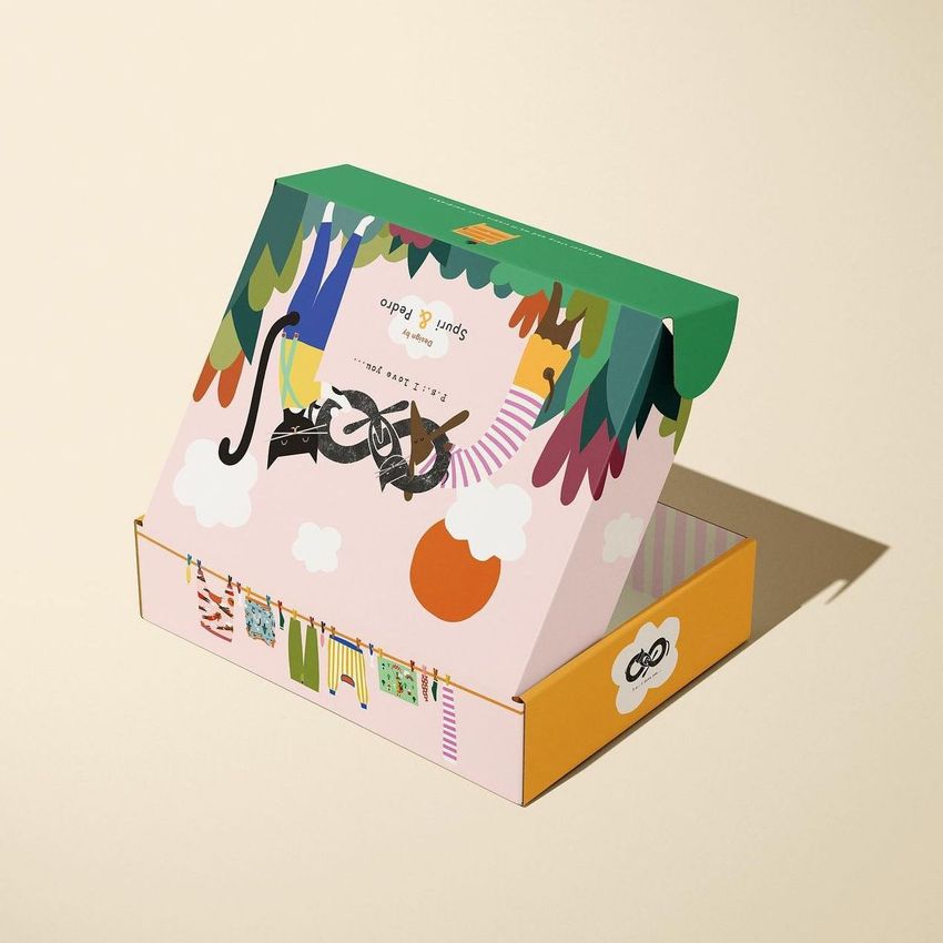 Colorful mailing box mockup with playful illustrated graphics, open on a neutral beige background, viewed from a high angle.